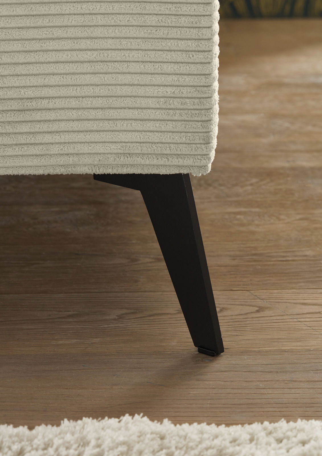 Nahaufnahme eines Polsterbettes mit strukturiertem Stoffbezug und schwarzem Holzbein, seitliche Perspektive.