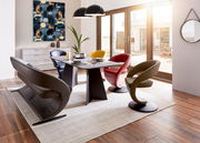 Moderner Essbereich mit einem rechteckigen Esstisch und farbigen Sesseln in einem hellen Raum mit großen Fenstern, seitliche Perspektive.