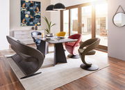 Moderner Essbereich mit einem rechteckigen Esstisch und farbigen Sesseln in einem hellen Raum mit großen Fenstern, seitliche Perspektive.