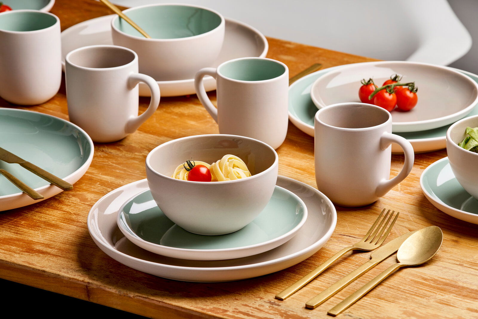 Kombiservice 16-tlg. in moderner Tischansicht mit Tellern, Schalen und Tassen in Weiß und Mintgrün, dekoriert mit goldfarbenem Besteck und frischen Zutaten.