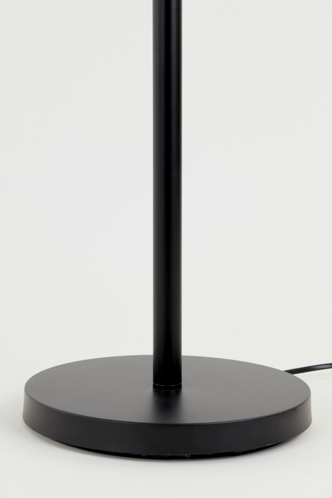 Close-up van de voet van een zwarte staande lamp met ronde voet, gezien vanaf de zijkant.