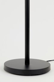 Close-up van de voet van een zwarte staande lamp met ronde voet, gezien vanaf de zijkant.