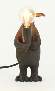 Tischleuchte in Form eines Pinguins, der eine Glühbirne hält, frontal betrachtet.