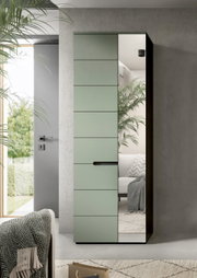 Moderner Kleiderschrank mit mattgrüner Front und vertikaler Spiegeltür, schwarzem Griff und Korpus, im Wohnzimmer platziert; Perspektive: frontale Ansicht mit leichter Rechtsansicht.