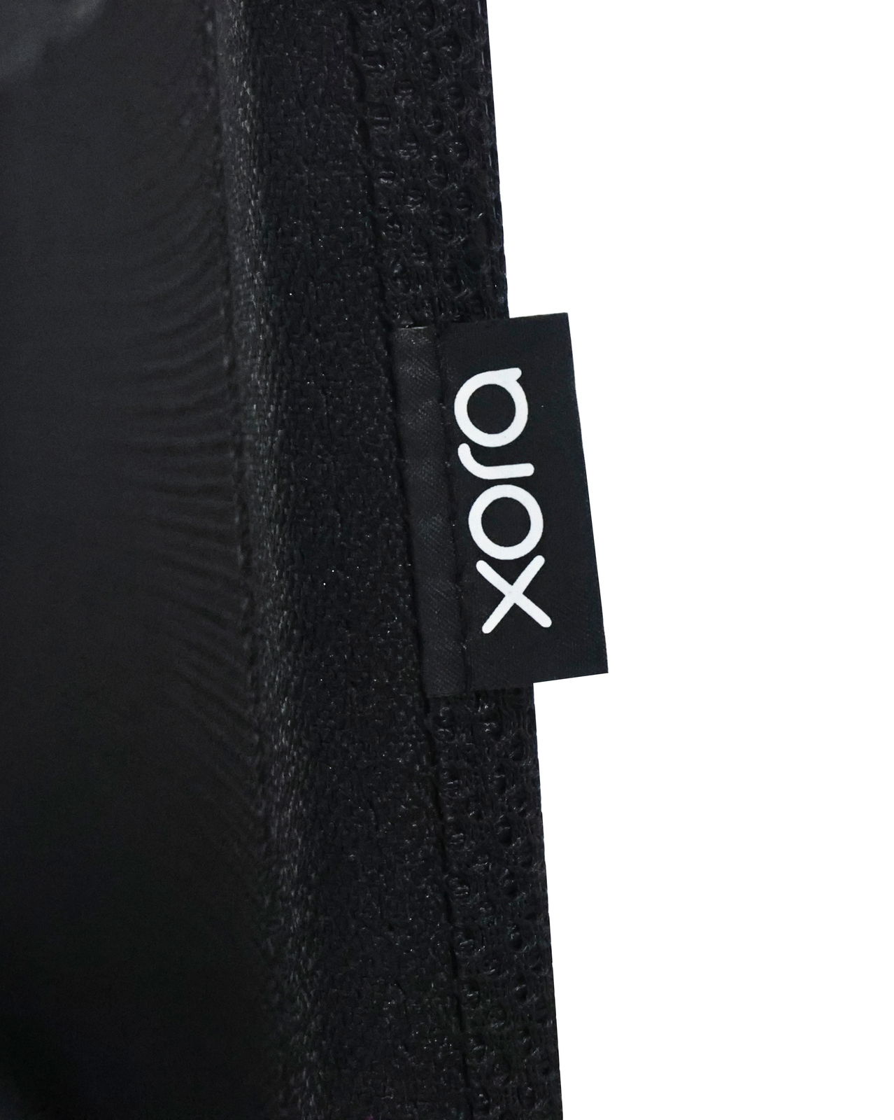 Nahaufnahme eines schwarzen Stoffes mit einem Etikett der Marke 'xora', seitliche Perspektive.