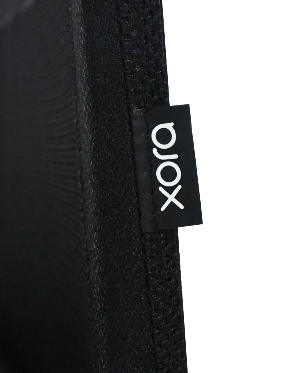 Nahaufnahme eines schwarzen Stoffes mit einem Etikett der Marke 'xora', seitliche Perspektive.