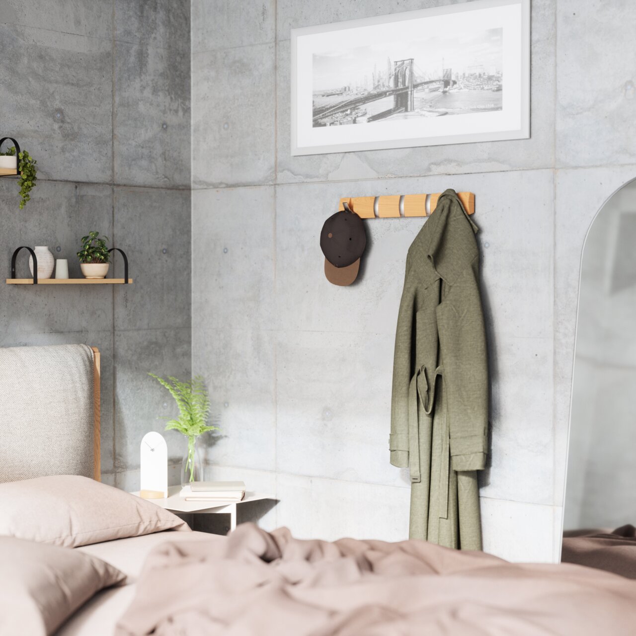 Wandgarderobe aus Holz mit mehreren Haken, an der eine grüne Jacke und eine braune Kappe hängen, in einem modernen Schlafzimmer mit Betonwänden. Perspektive von der Seite.