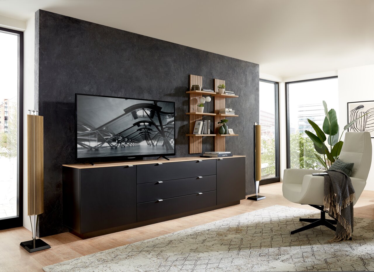 Modernes Wohnzimmer mit einem eleganten Wandpaneel, das als Hintergrund für ein TV-Gerät und ein Regal mit Dekorationen dient. Perspektive von vorne.