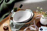 Zwei weiße Pastaschalen in einem Korb, umgeben von Olivenölflasche, Kräutern und Dekoration, aus der Vogelperspektive fotografiert.