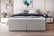 Modernes graues Boxspringbett mit gepolstertem Kopfteil, schwarz-grauer Bettwäsche und dekorativen Kissen im stilvollen Schlafzimmer, frontal von vorne aus Augenhöhe fotografiert.