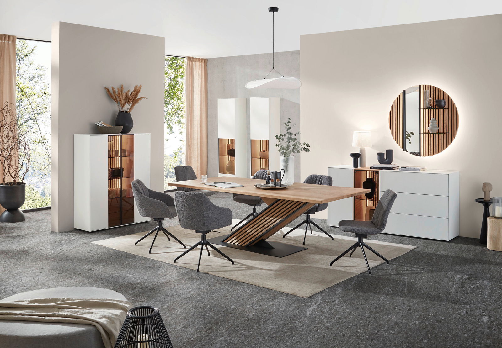 Moderne Esszimmer-Einrichtung mit einem großen Holztisch und grauen Stühlen, flankiert von weißen Vitrinen und einem Sideboard. Perspektive von vorne auf den Tisch und die Stühle.