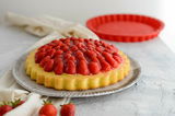Silikon-Obstkuchenform in Rot, 28 cm, mit einem gebackenen Obstkuchen mit Erdbeeren im Vordergrund, seitliche Perspektive