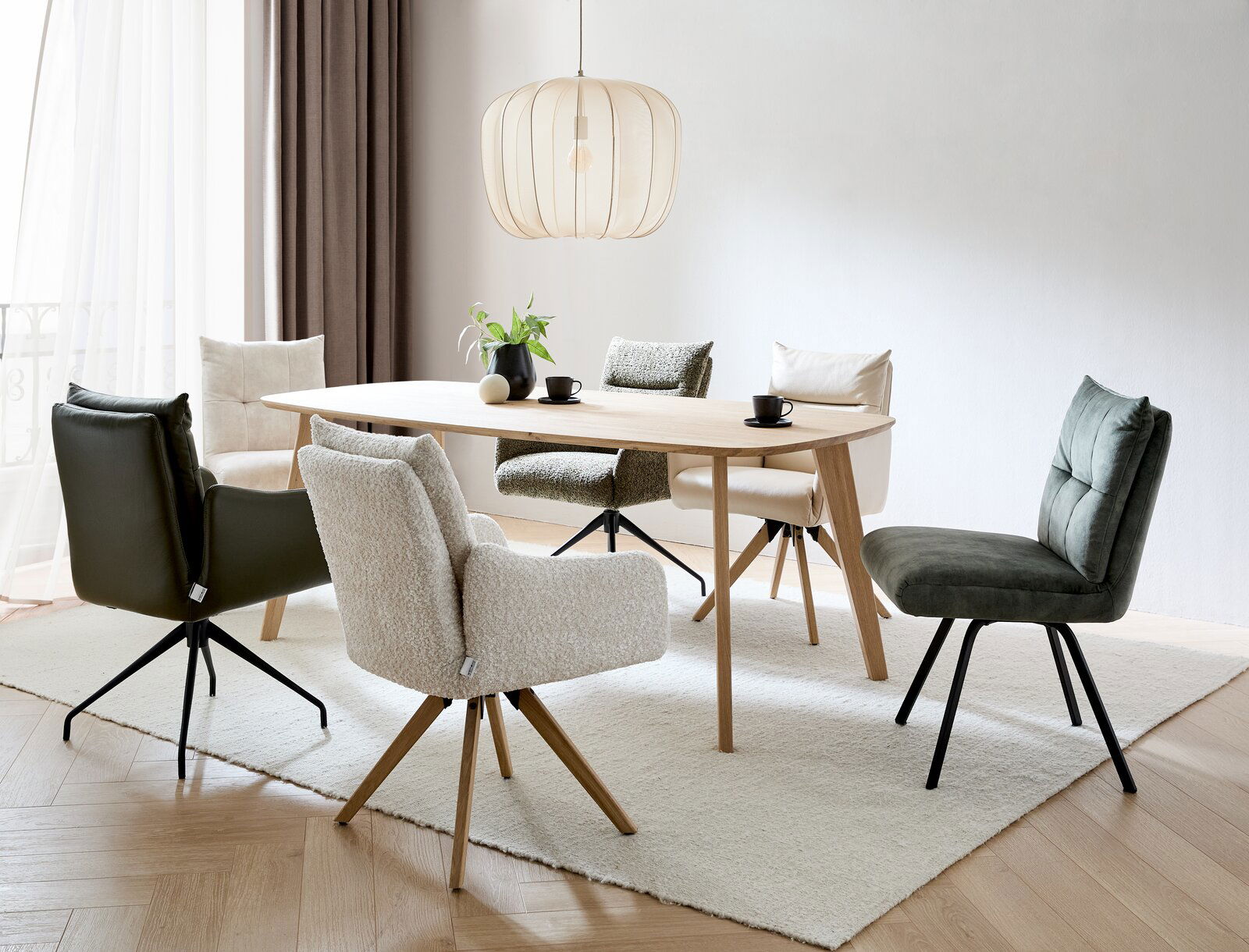 Moderner Esstisch aus Holz mit verschiedenen gepolsterten Stühlen in einem hellen Raum, seitliche Perspektive.