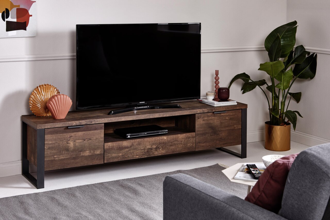 Jahnke TV-Möbel LOOP TV-Möbel aus dunklem Holz mit Metallrahmen, darauf ein großer Fernseher, dekoriert mit Vasen und Pflanzen, Perspektive von vorne.