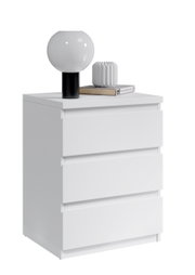 Weiße Nachtkommode mit drei Schubladen, darauf eine moderne Lampe und Dekoration, seitliche Perspektive
