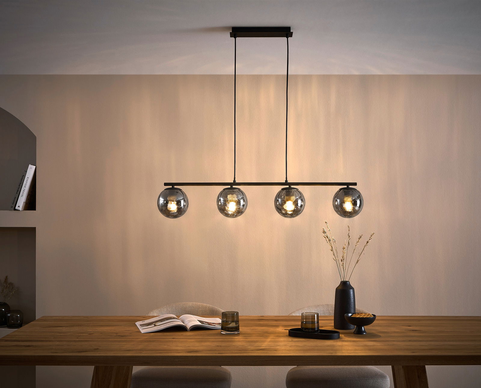 Moderne Hängeleuchte mit vier kugelförmigen, rauchgrauen Glaskörpern über einem Esstisch, seitliche Perspektive.