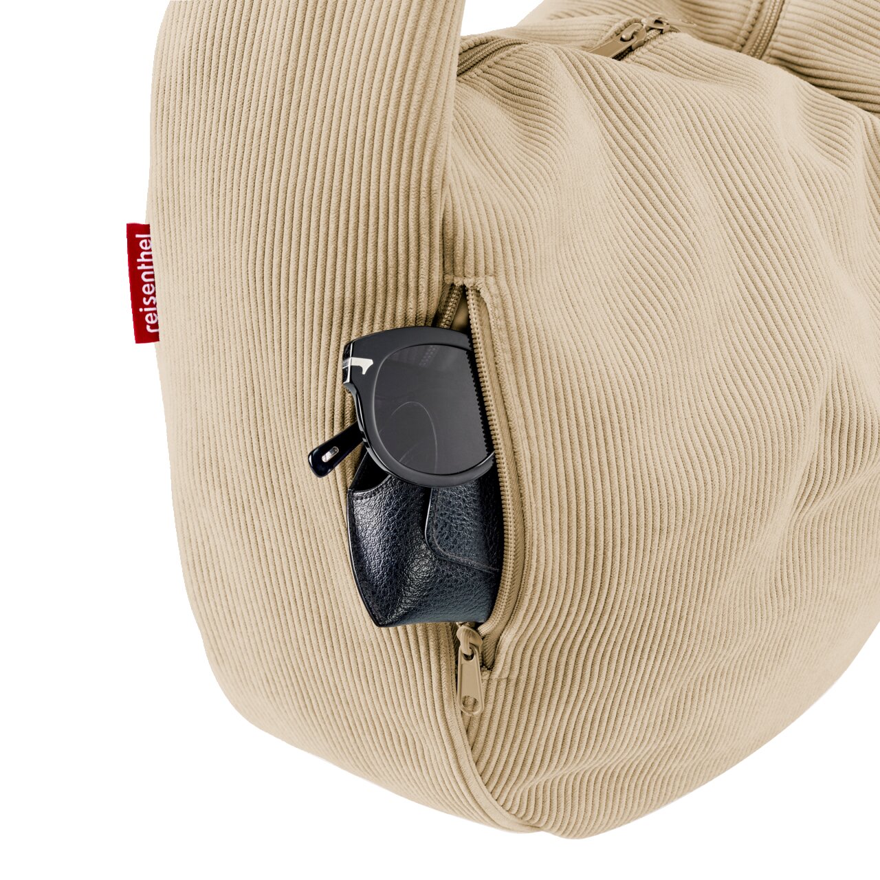 Beige Cord-Reisetasche mit seitlicher Reißverschlusstasche, aus der Sonnenbrille und schwarzes Etui herausragen, Nahaufnahme in seitlicher Perspektive.