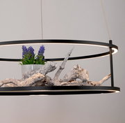 Moderne LED-Pendelleuchte mit schwarzem Rahmen, dekoriert mit Holz und lila Blumen, seitliche Perspektive.