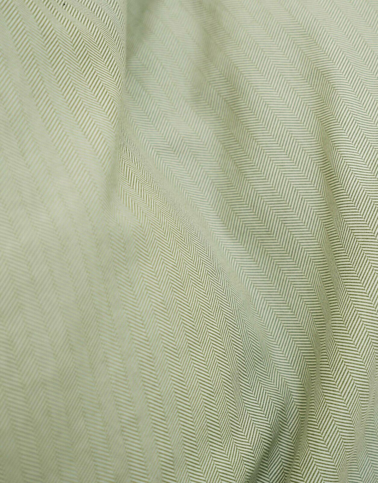 Nahaufnahme einer Bettwäsche mit Fischgrätenmuster in sanftem Grün.