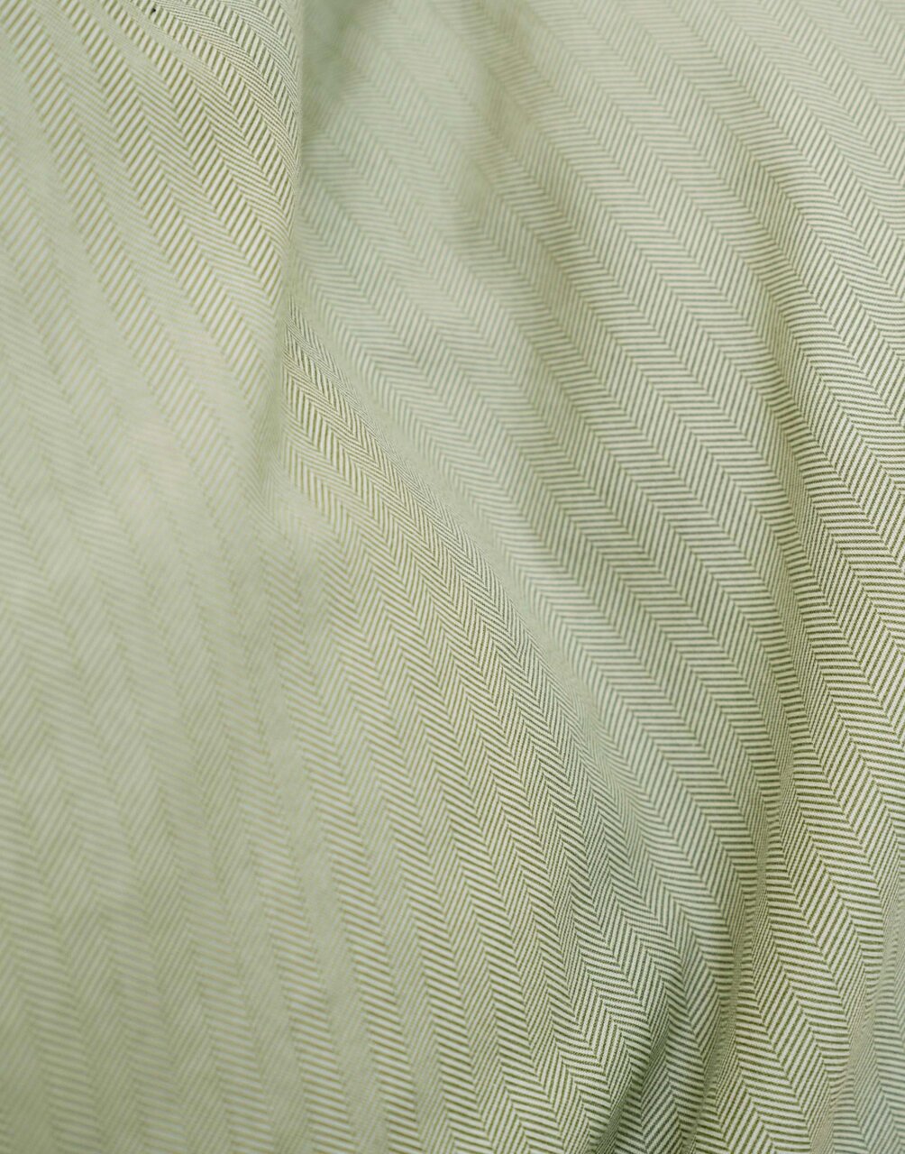 Nahaufnahme einer Bettwäsche mit Fischgrätenmuster in sanftem Grün.