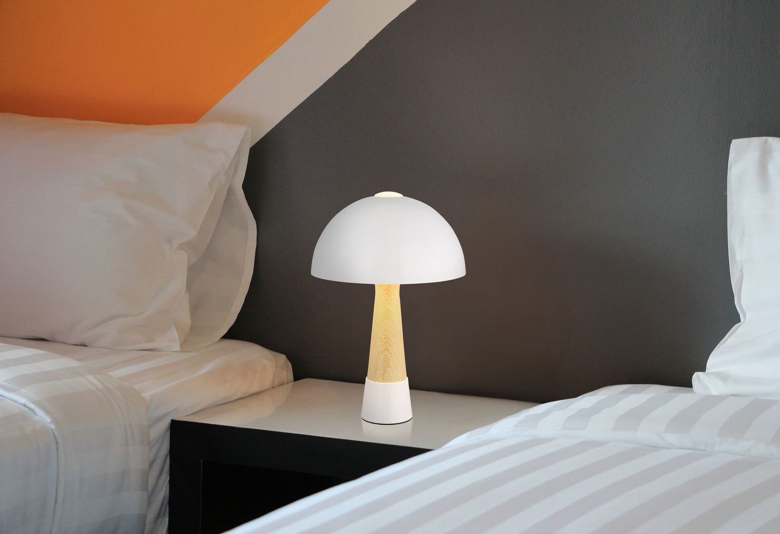 Moderne Tischleuchte mit weißem Schirm und Holzfuß, seitlich auf einem Nachttisch zwischen zwei Betten platziert.