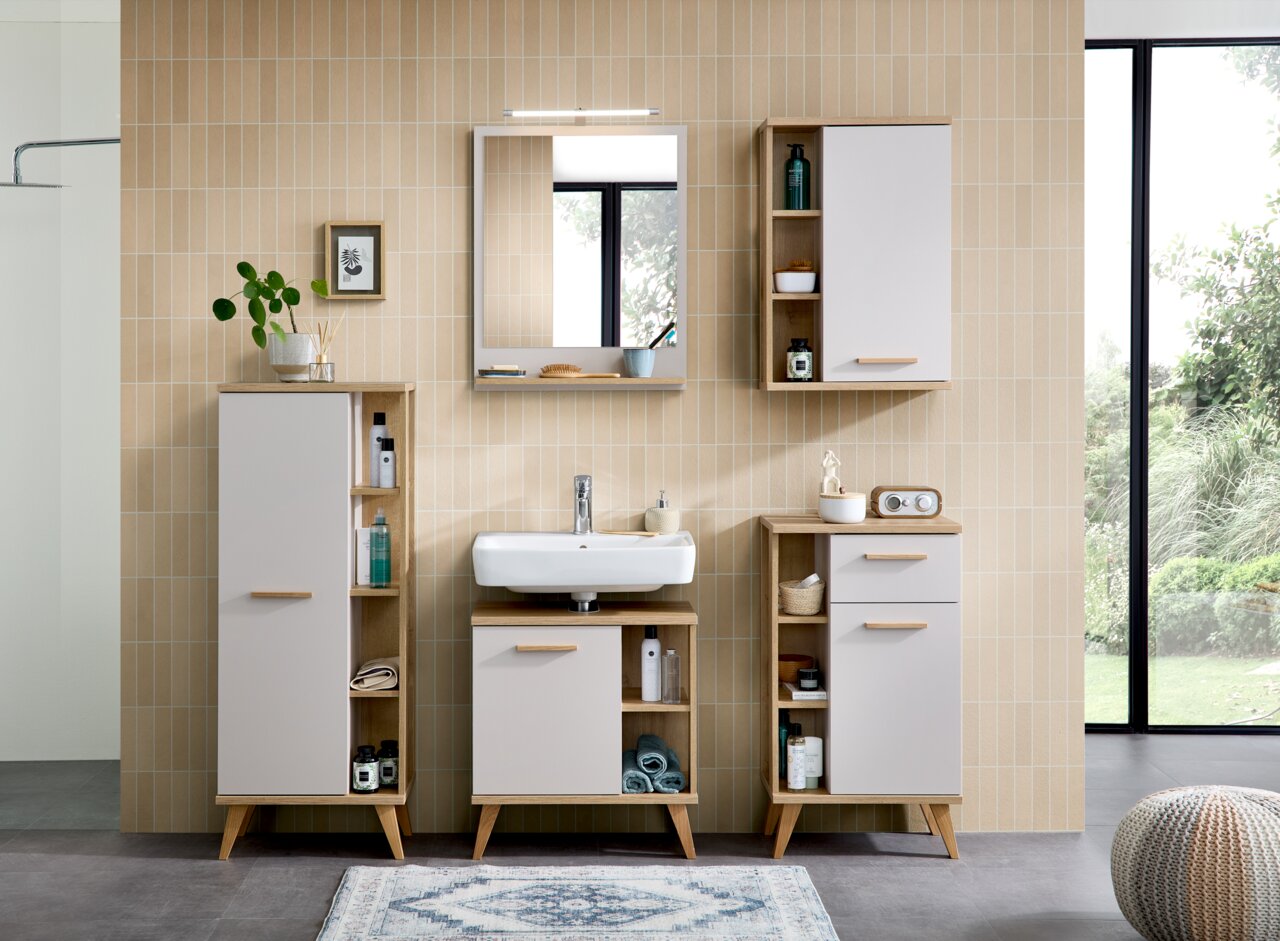 Badezimmer mit moderner Einrichtung, bestehend aus einem Waschbecken mit Unterschrank, einem Spiegel mit TwinLED-Aufsatzleuchte und mehreren Schränken in Holzoptik. Frontalansicht.