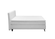 Seitliche Ansicht eines modernen Boxspringbetts in Weiß mit schlichtem Design und schwarzen Füßen.