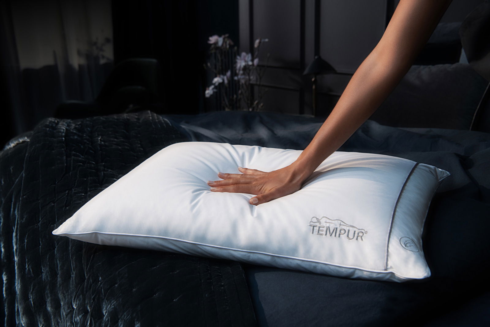 Hand drückt auf ein weißes Schlafkissen auf einem Bett, seitliche Perspektive