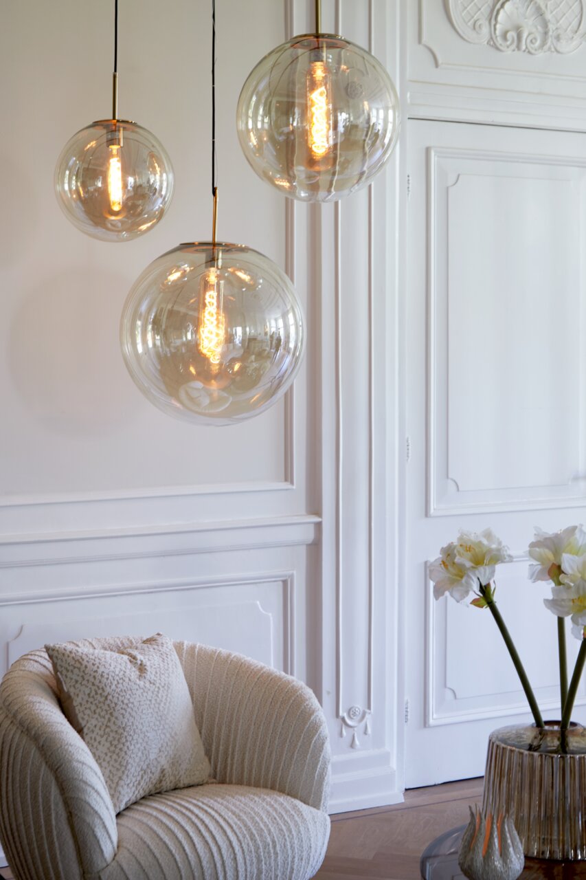 Drei elegante Hängeleuchten aus Glas in einem stilvollen Raum, von der Seite betrachtet.