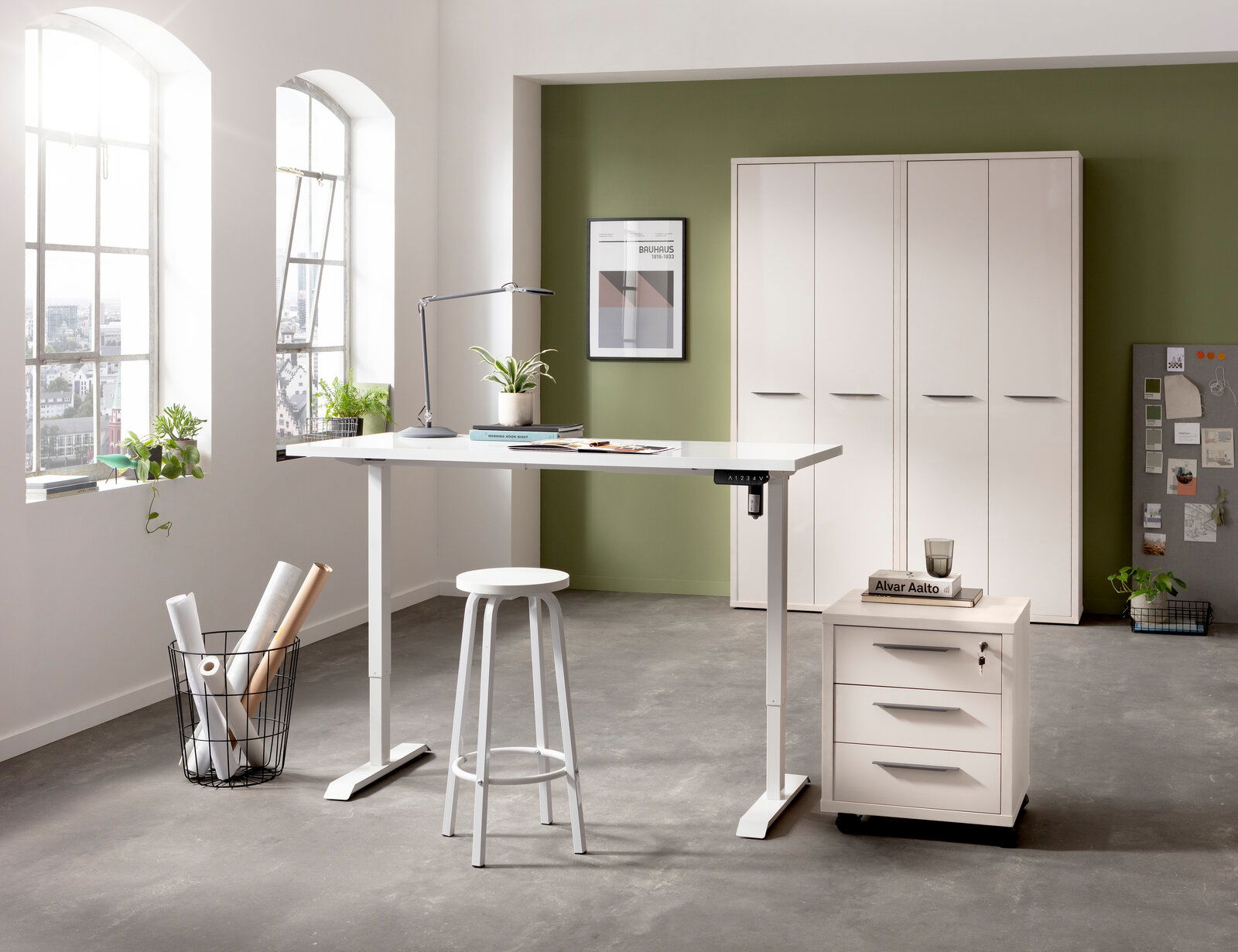 Moderner höhenverstellbarer Schreibtisch in einem hellen Büro mit Blick auf Fenster und Schränke im Hintergrund.