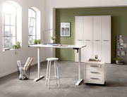 Moderner höhenverstellbarer Schreibtisch in einem hellen Büro mit Blick auf Fenster und Schränke im Hintergrund.