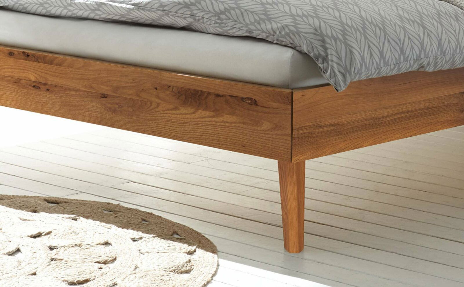 Nahaufnahme eines Bettgestells aus Holz mit Bettdecke, seitliche Perspektive