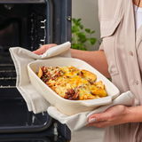 Eine Person hält eine Auflaufform mit Deckel, gefüllt mit überbackenen Nachos, aus dem Ofen. Die Perspektive zeigt die Auflaufform von vorne.