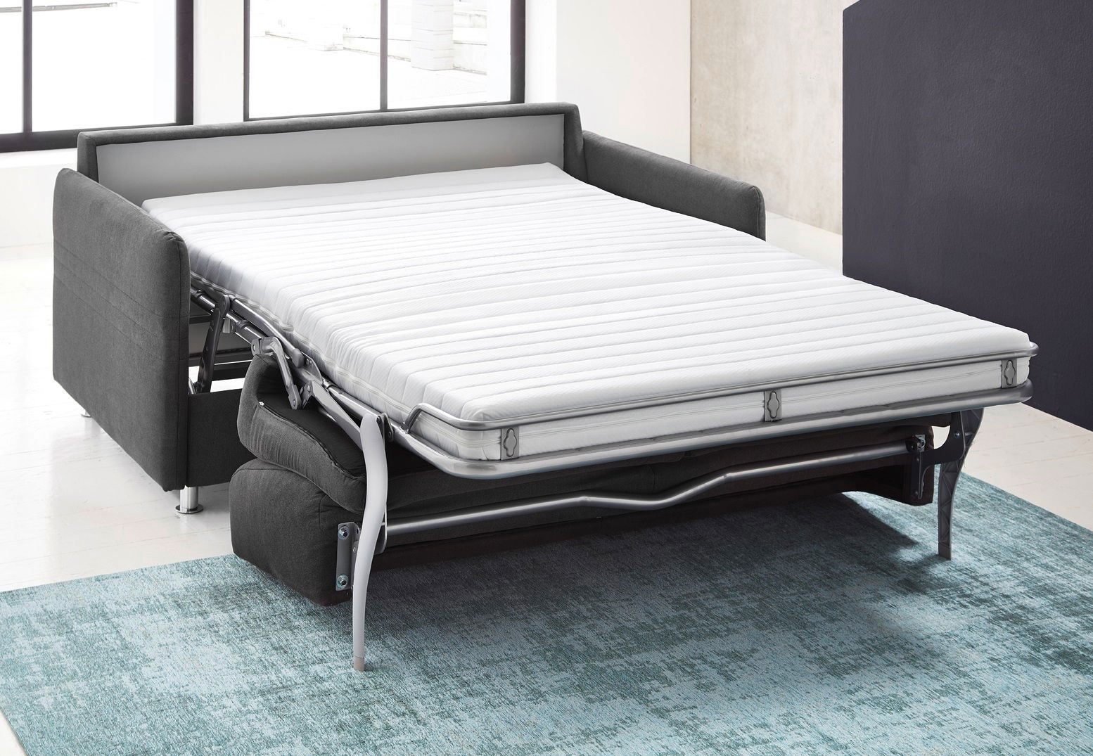 Schlafsofa in ausgeklappter Position, seitliche Perspektive, auf einem blauen Teppich stehend.