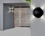 Moderne LED-Außenwandleuchte in schwarzem Design, montiert an einer grauen Wand neben einer Glastür, mit Lichtstrahlen in alle Richtungen.