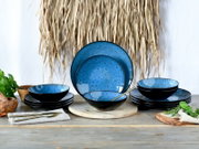 Blau-schwarzes Keramik-Geschirrset mit Tellern und Schalen auf Holztisch dekoriert mit Kräutern, Frontalansicht auf das Arrangement