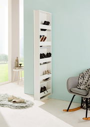 Schmaler, weißer Drehschuhschrank mit mehreren Fächern, gefüllt mit Schuhen, in einem modernen, hellen Raum mit Blick auf eine grüne Landschaft. Perspektive von der Seite.