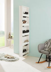 Schmaler, weißer Drehschuhschrank mit mehreren Fächern, gefüllt mit Schuhen, in einem modernen, hellen Raum mit Blick auf eine grüne Landschaft. Perspektive von der Seite.