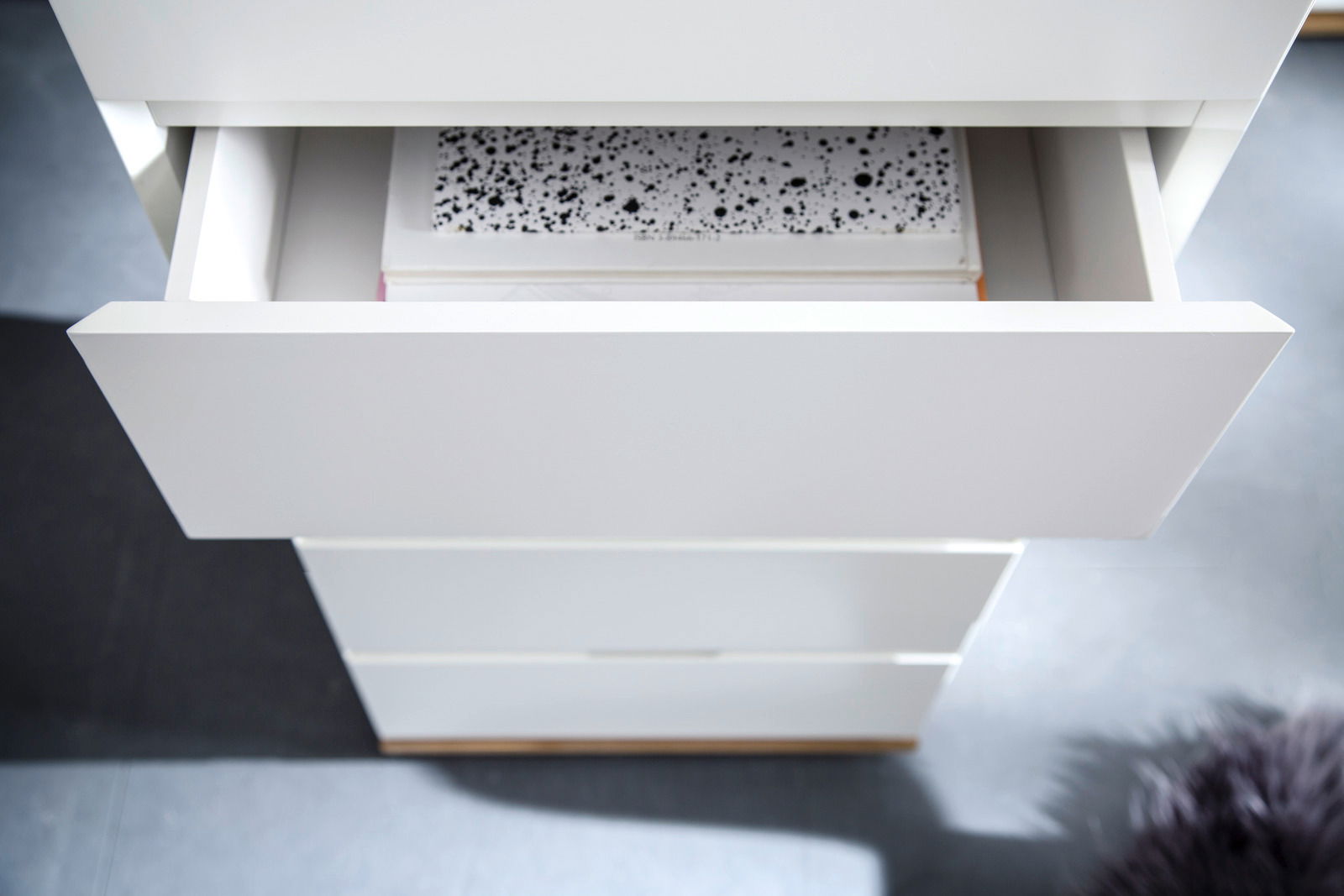 Hochkommode CHIARO in Weiß mit geöffneter Schublade, von oben fotografiert.