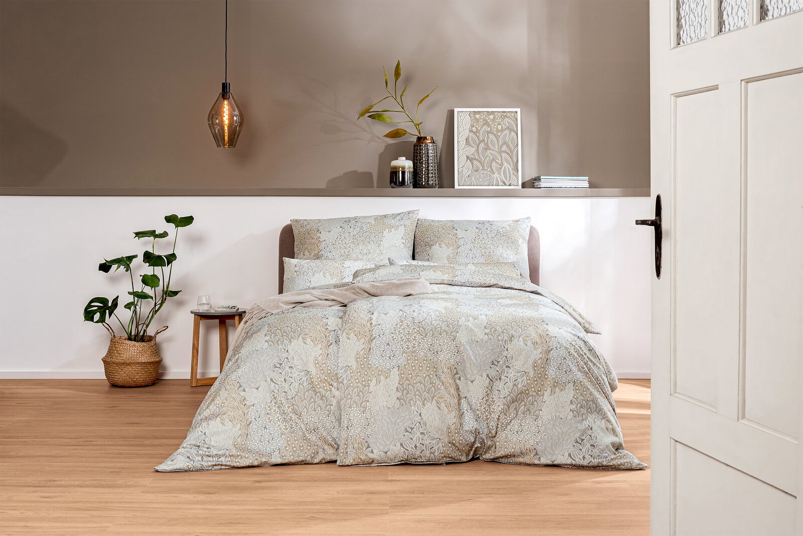 Bettwäsche-Set in sanften Beige- und Grautönen mit floralem Muster, auf einem Bett in einem stilvoll eingerichteten Schlafzimmer, aus der Perspektive durch eine geöffnete Tür betrachtet.