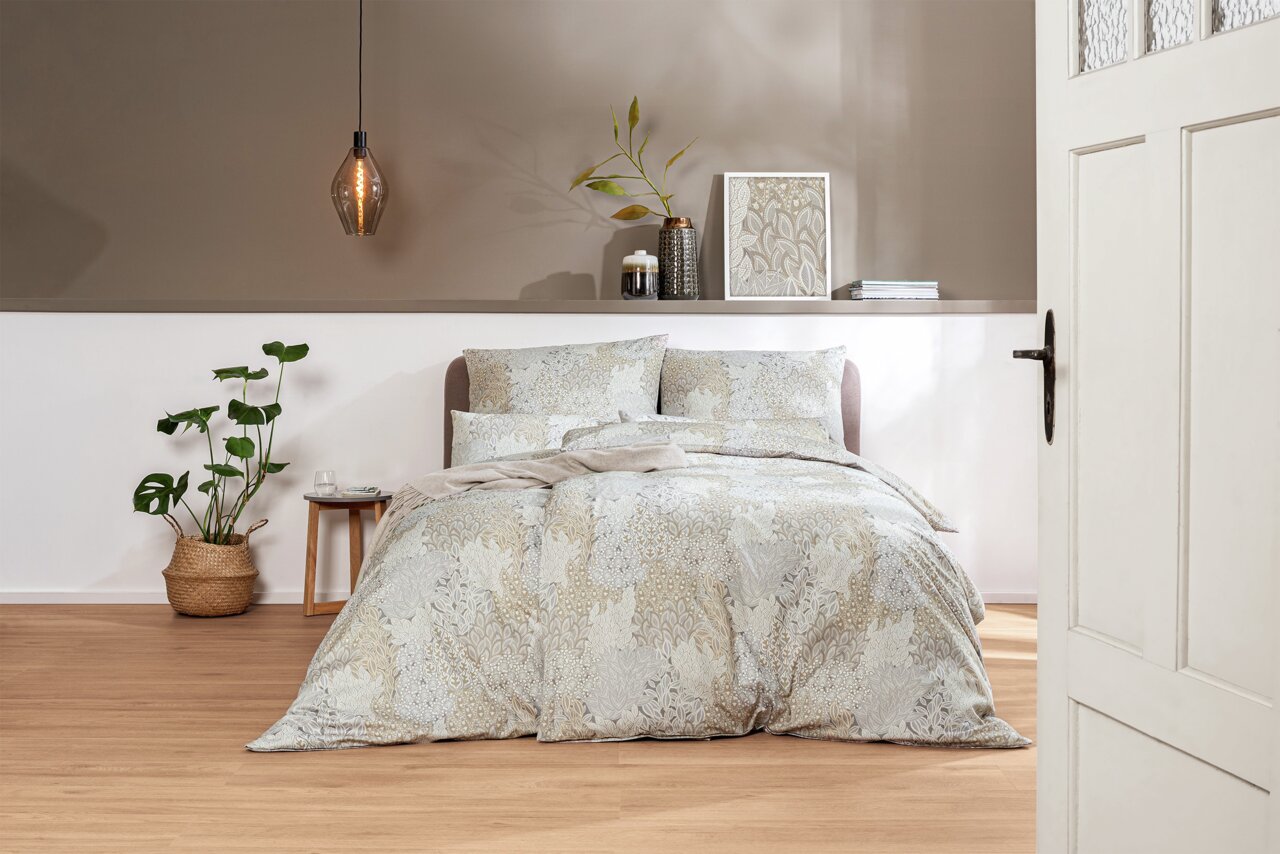 Bettwäsche-Set in sanften Beige- und Grautönen mit floralem Muster, auf einem Bett in einem stilvoll eingerichteten Schlafzimmer, aus der Perspektive durch eine geöffnete Tür betrachtet.