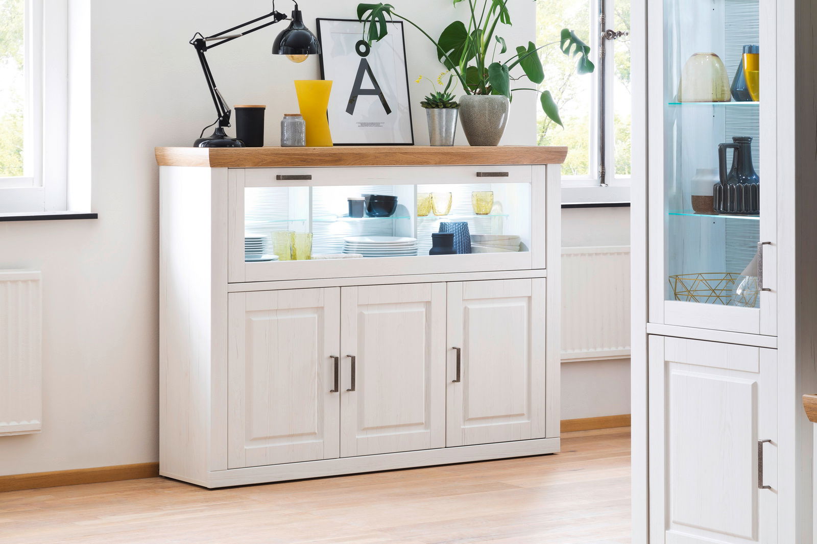 Landscape Highboard BREGENZ Weißes Highboard mit Holzplatte, dekoriert mit Pflanzen und Lampen, aus frontaler Perspektive fotografiert.