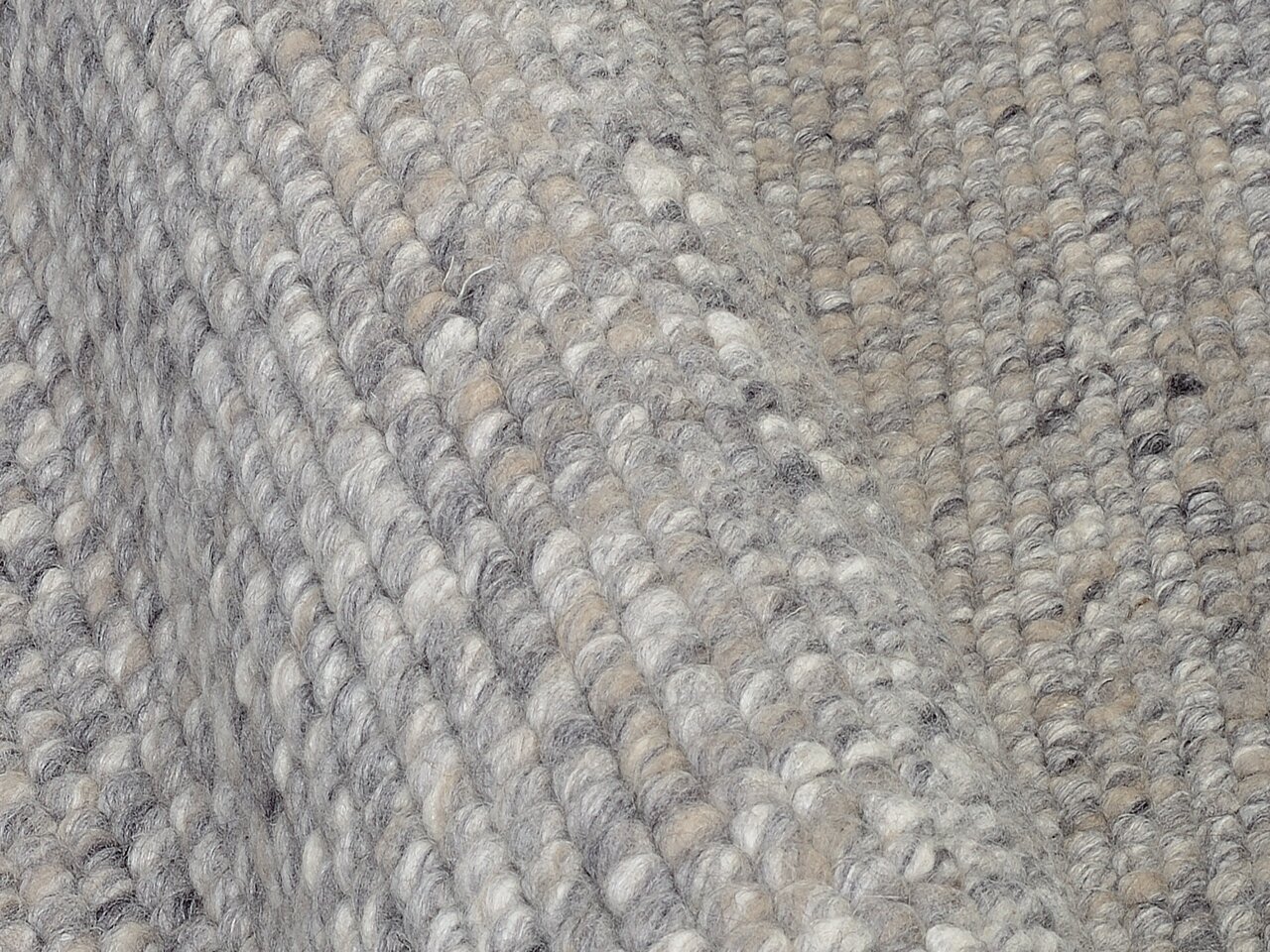 Nahaufnahme eines handgewebten Teppichs in Grautönen mit strukturierter Oberfläche, seitliche Perspektive.
