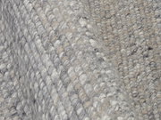Nahaufnahme eines handgewebten Teppichs in Grautönen mit strukturierter Oberfläche, seitliche Perspektive.