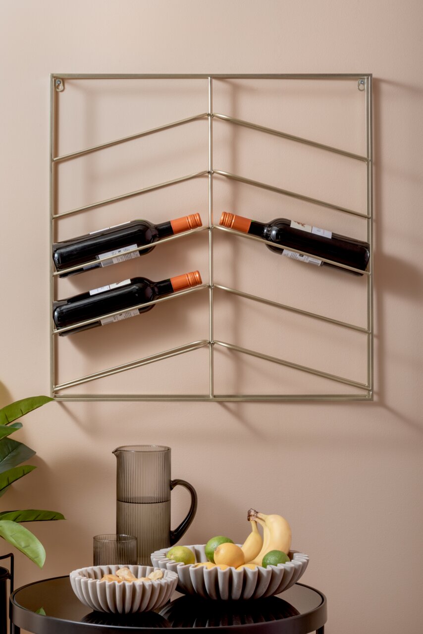 Wandregal mit Weinflaschen, darunter ein Tisch mit einer geriffelten Glaskaraffe, einem Glas und zwei weißen Schalen, gefüllt mit Obst und Snacks. Perspektive von vorne.