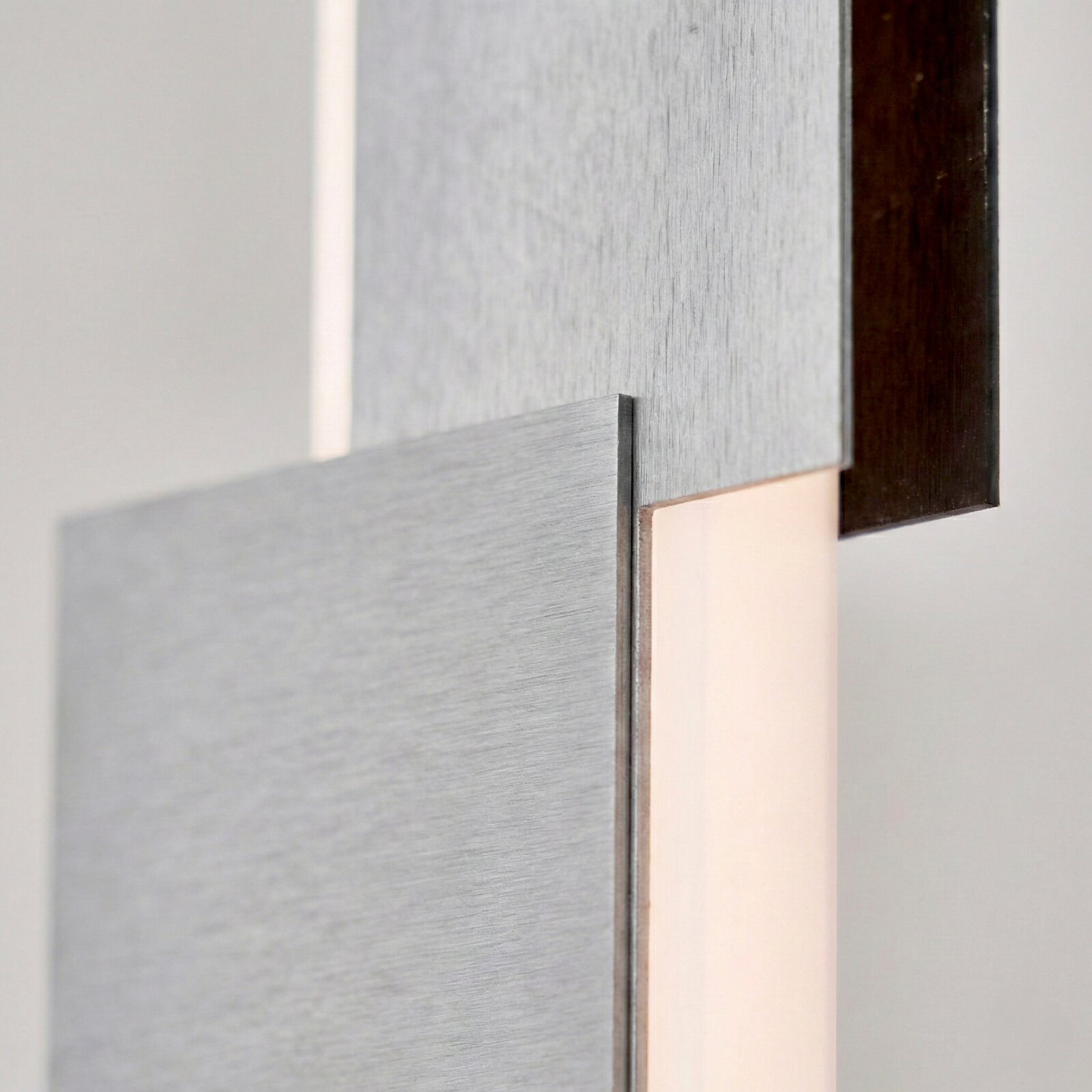 Detailansicht aus seitlicher Nahperspektive einer modernen Wandleuchte mit geometrisch überlagerten Paneelen aus gebürstetem Metall und warmem, indirektem Licht.
