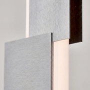 Detailansicht aus seitlicher Nahperspektive einer modernen Wandleuchte mit geometrisch überlagerten Paneelen aus gebürstetem Metall und warmem, indirektem Licht.