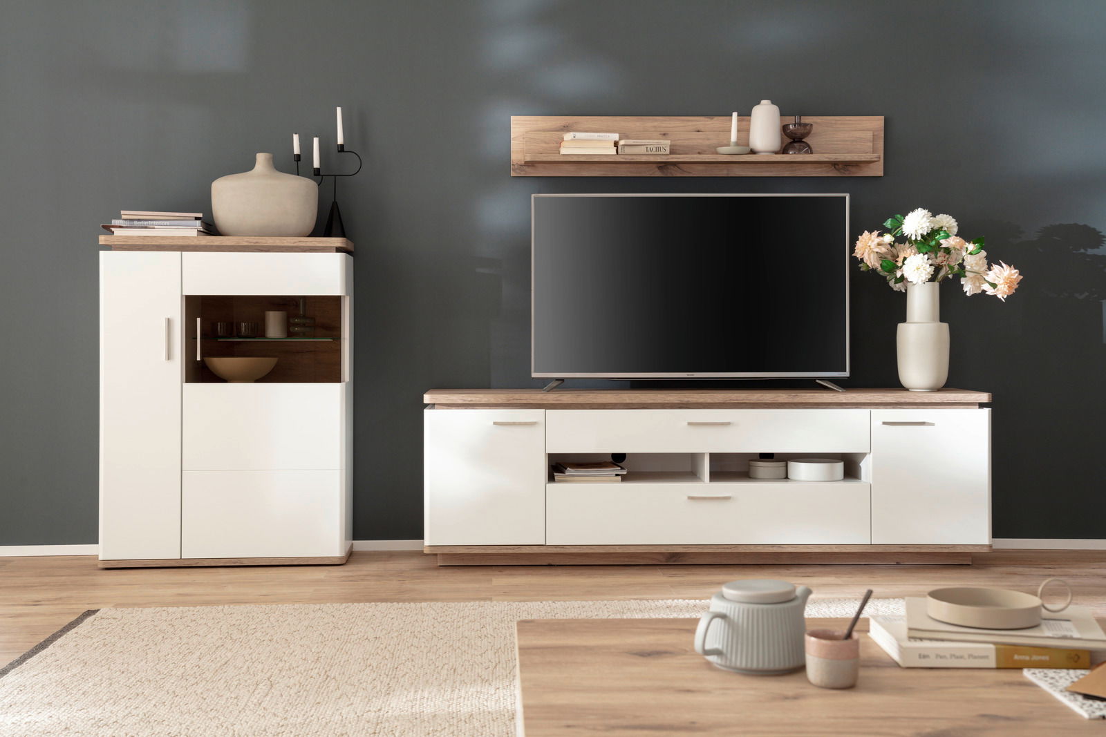 Moderne Wandkombination in hellem Holz und Weiß, bestehend aus einem TV-Schrank, einem Hängeregal und einem Schrank, frontal fotografiert.