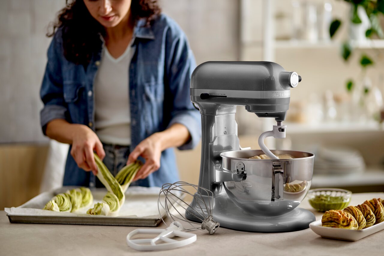 KitchenAid Keukenmachine HEAVY DUTY 5KSM55SXXECU Heavy Duty-keukenmachine van 5,2 liter in een moderne keuken, gezien vanaf de zijkant, terwijl iemand deeg aan het bereiden is.