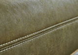 Nahaufnahme einer olivgrünen Lederoberfläche mit weißen Ziernähten, seitliche Perspektive.